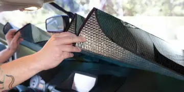 Mani che posizionano un parasole riflettente sul cruscotto per proteggere l'auto dal sole.