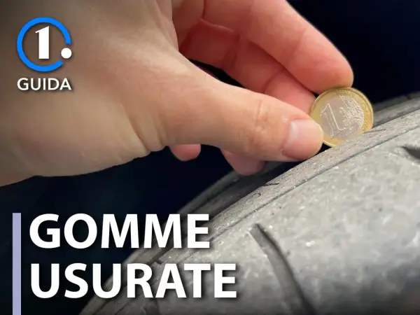 Una mano tiene una moneta da 1 euro per controllare il battistrada di pneumatici usurati. La guida mostra come verificare la sicurezza.